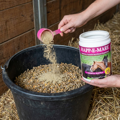 Happ-E-Mare,"Hand pouring powder scoop into feed tub beside supplement container"